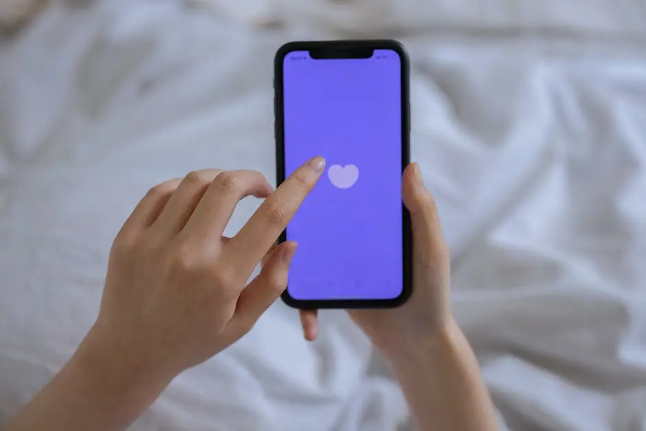 Close-up of hands using a smartphone with a heart icon on screen, representing technology and connection.