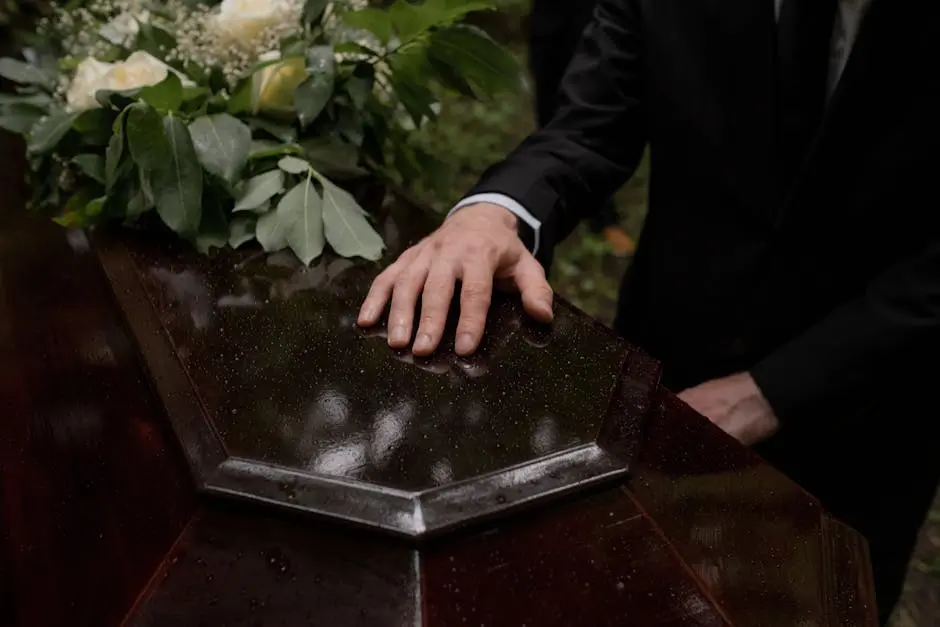 A hand placed on a coffin with flowers, symbolizing loss and mourning.