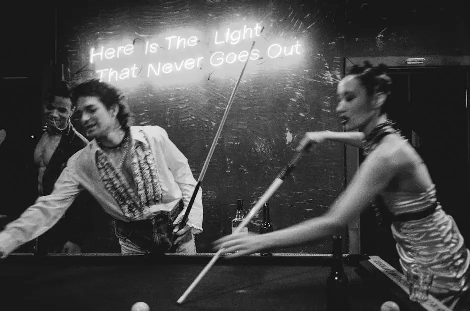 A lively black and white image capturing people playing billiards under neon lights in a bar.