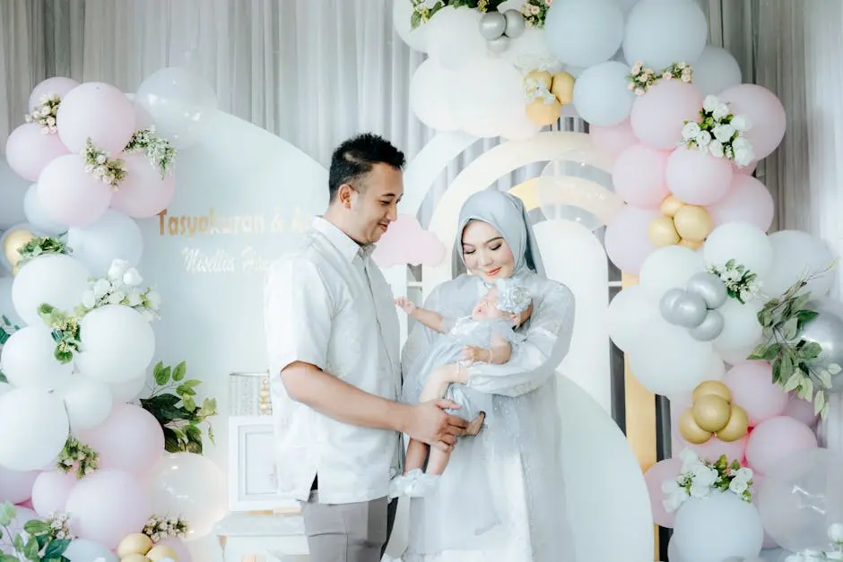 A family celebrating with pastel balloons, parents in elegant attire holding their baby.