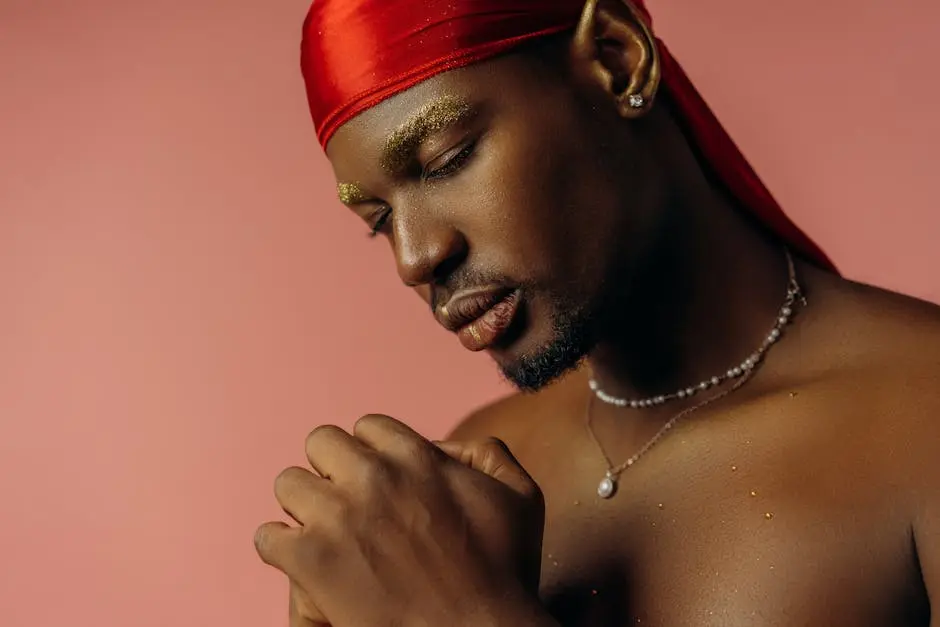 Close-up of a fashionable man with jewelry against a soft pink background.