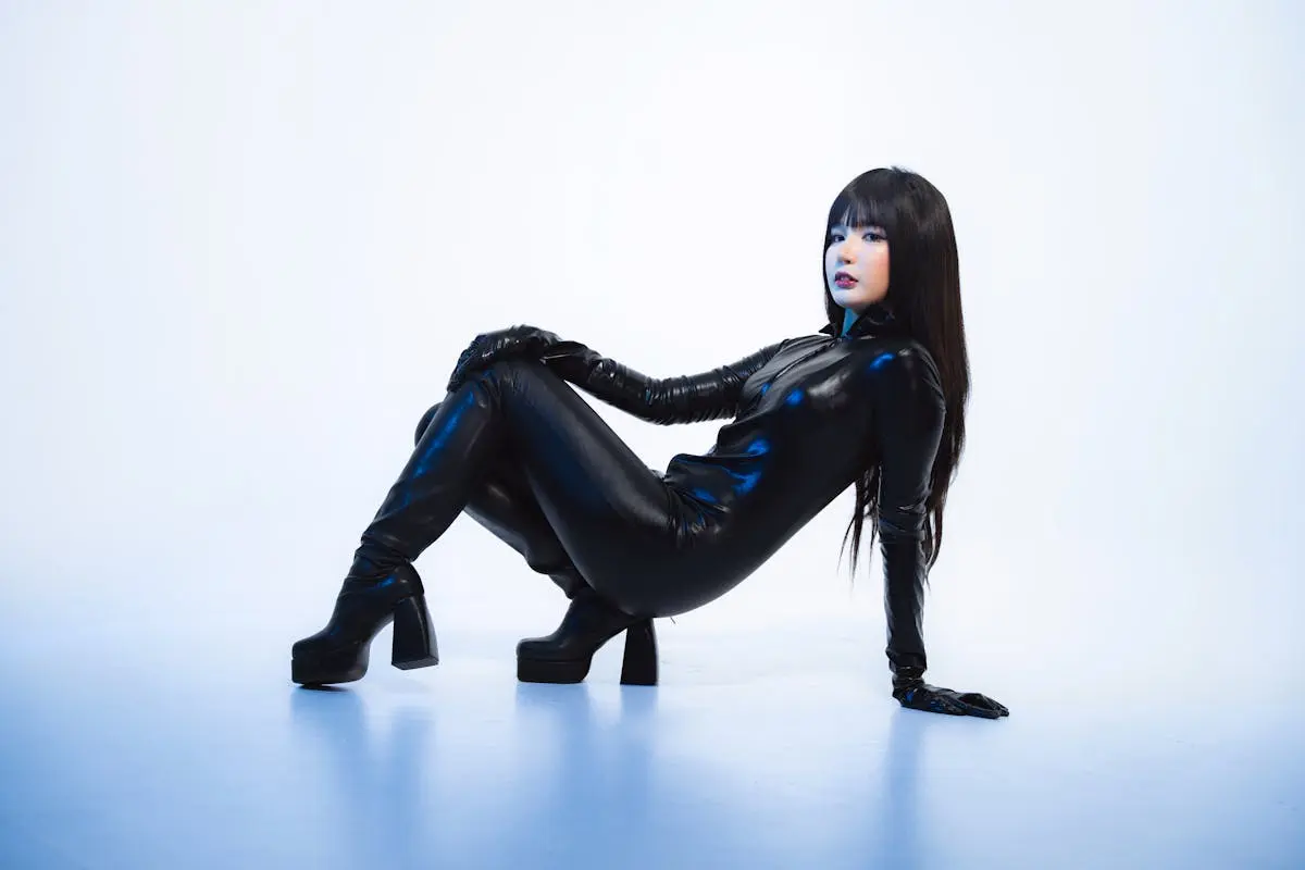 Woman posing in sleek black leather catsuit against minimal background.