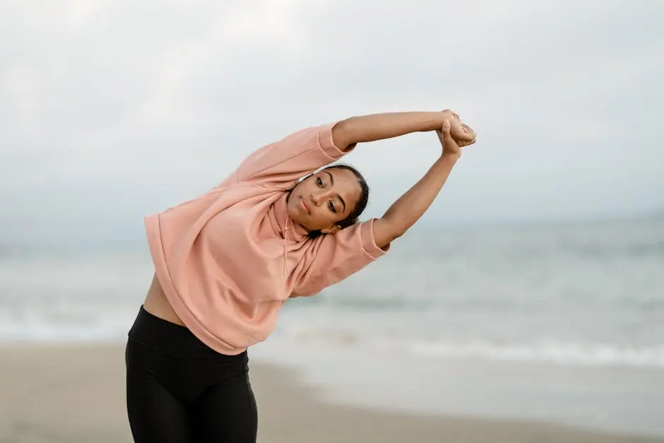 A woman performs a side stretch yoga pose on an ocean beach, promoting fitness and mindfulness.