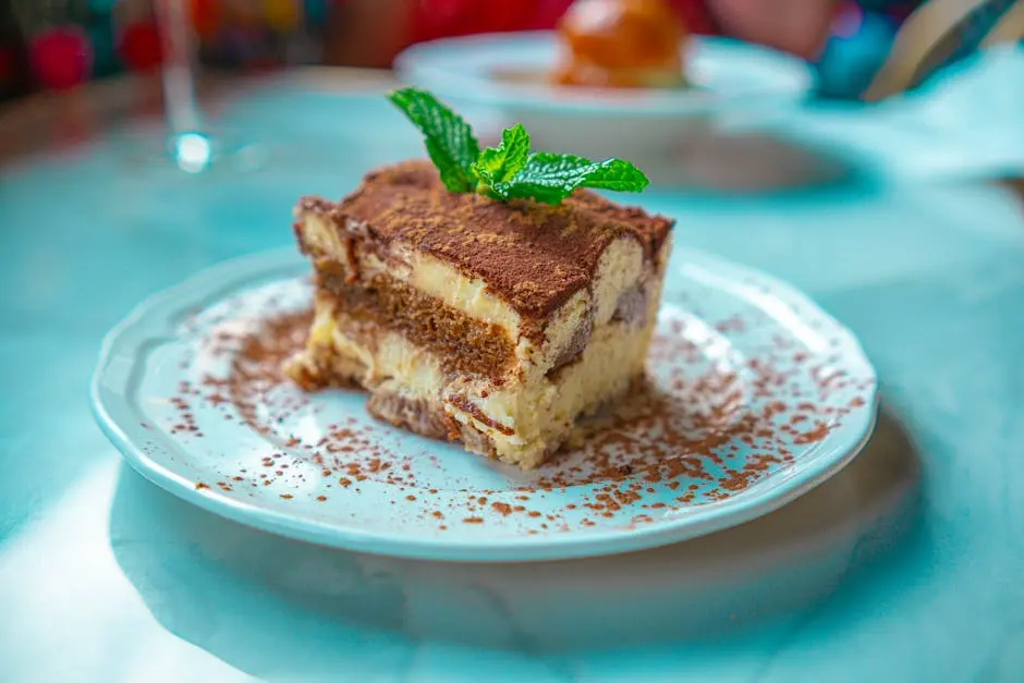 Mouth-watering slice of tiramisu with mint garnish on a white plate, perfect for dessert lovers.