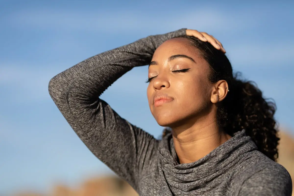 Close-up portrait of a woman enjoying sunlight with eyes closed, wearing a gray long sleeve shirt.