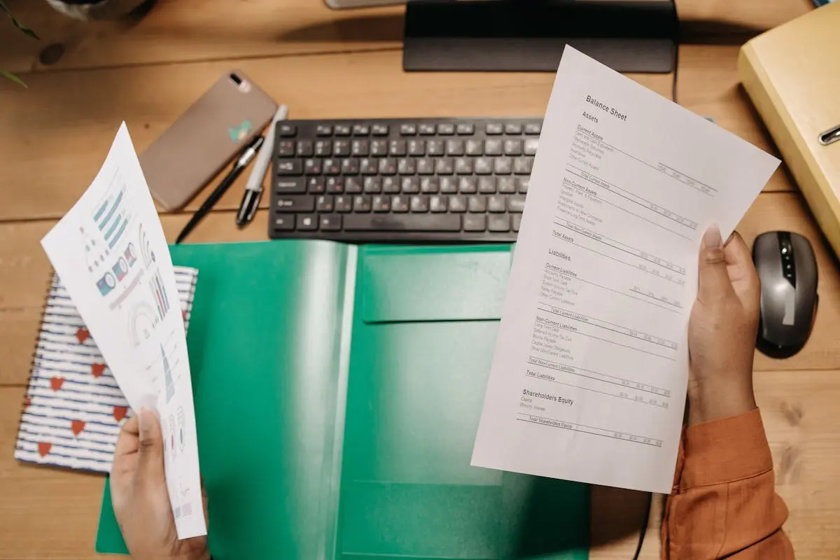Hands holding and reviewing cfo services pricing sheets over a desk with a keyboard and stationery.