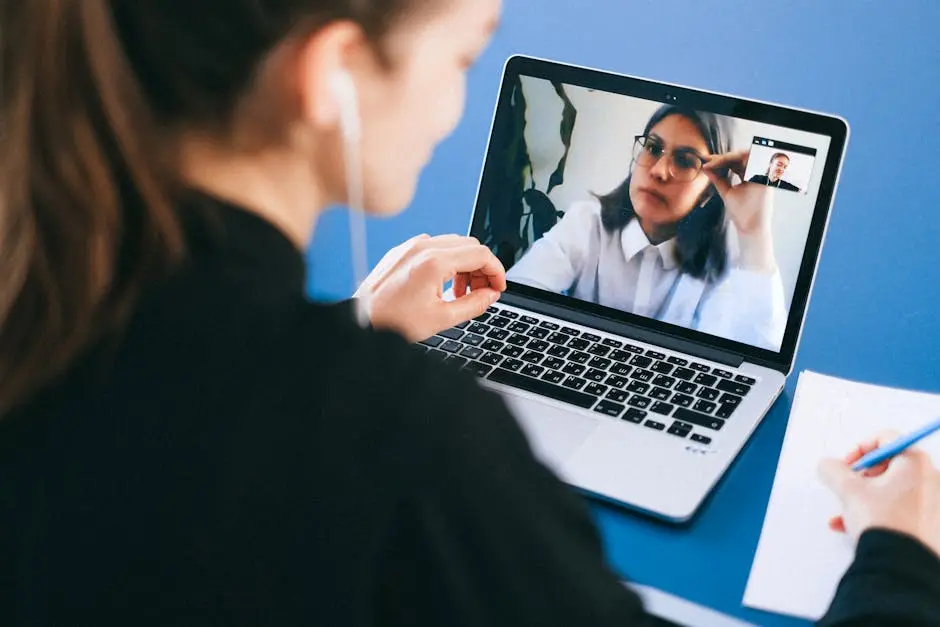 A woman engaged in a video conference call, taking notes during a professional meeting.