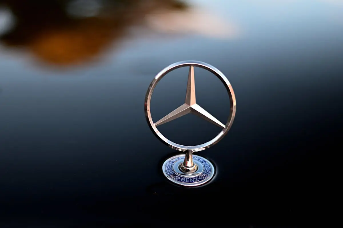 Close-up shot of a shiny Mercedes Benz logo emblem with reflective background, emphasizing luxury design.