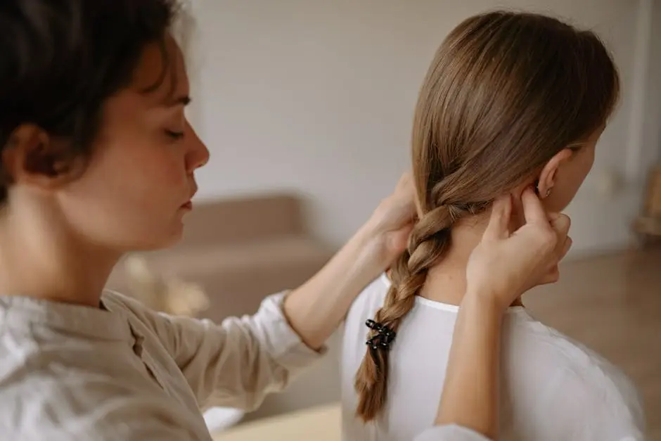Close-up of a woman braiding another woman’s hair indoors, evoking tranquility.