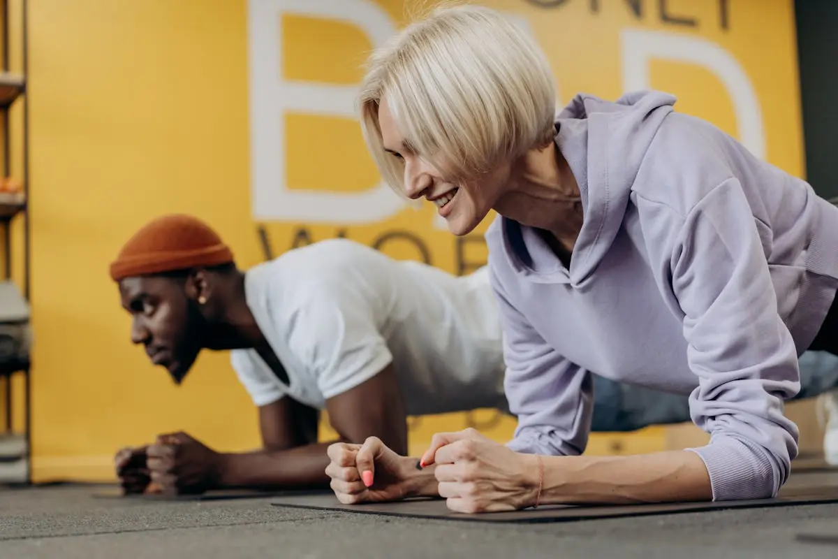 Two adults in sportswear doing plank exercises in a gym, focusing on strength and fitness.