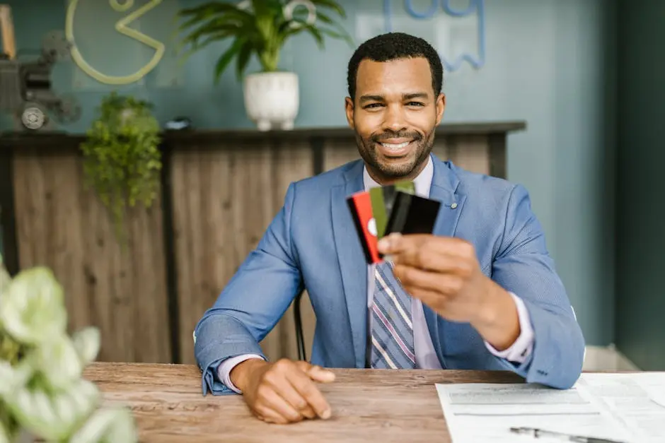Smiling African American man in a suit holding credit cards at a business desk.