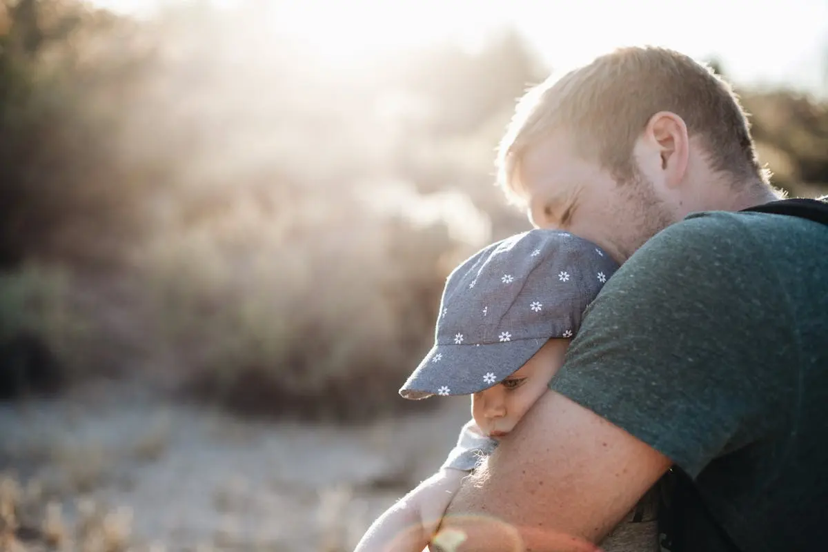 A father lovingly embraces his baby outdoors on a sunny day. Perfect for Father’s Day themes.