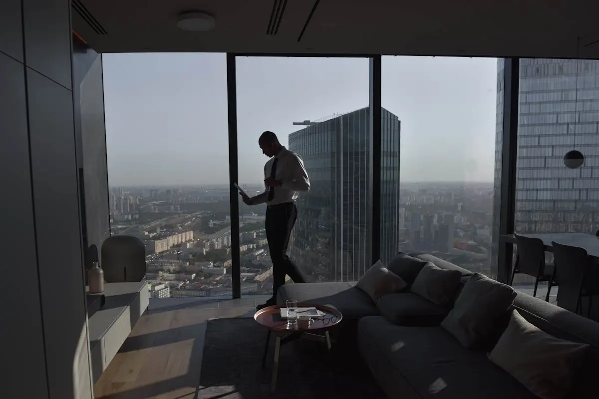Silhouette of a businessman standing in a luxury apartment with a panoramic cityscape view.