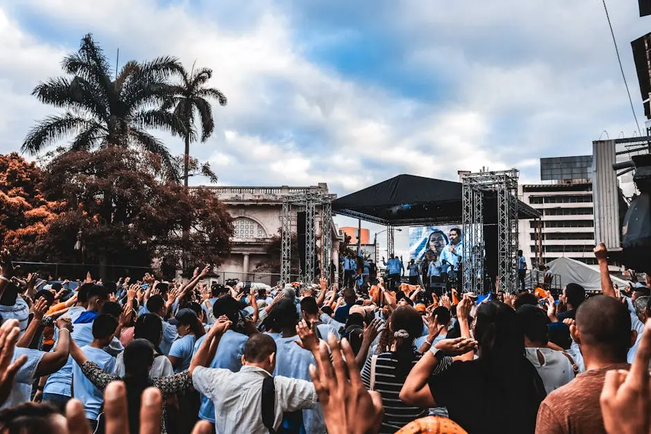 Dynamic scene at an outdoor concert with a large, enthusiastic crowd raising their hands.