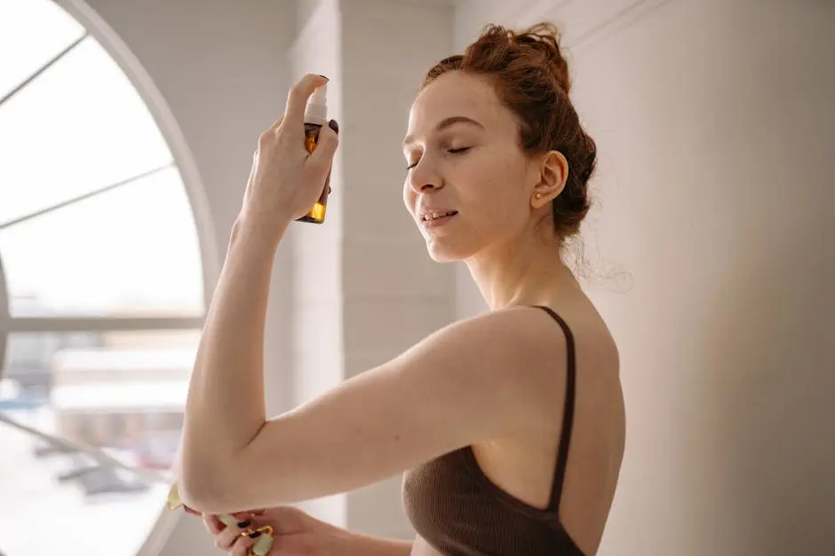 A woman enjoys a refreshing face mist in front of a large window, emphasizing skincare and self-care.