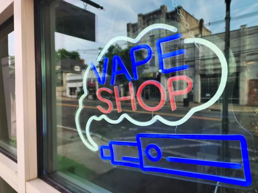 Bright neon sign of a vape shop in a city window reflecting the urban street.