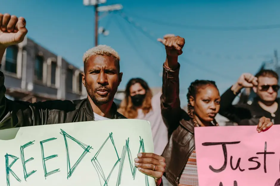A diverse crowd of adults protesting outdoors, holding signs and raising fists for freedom and justice.