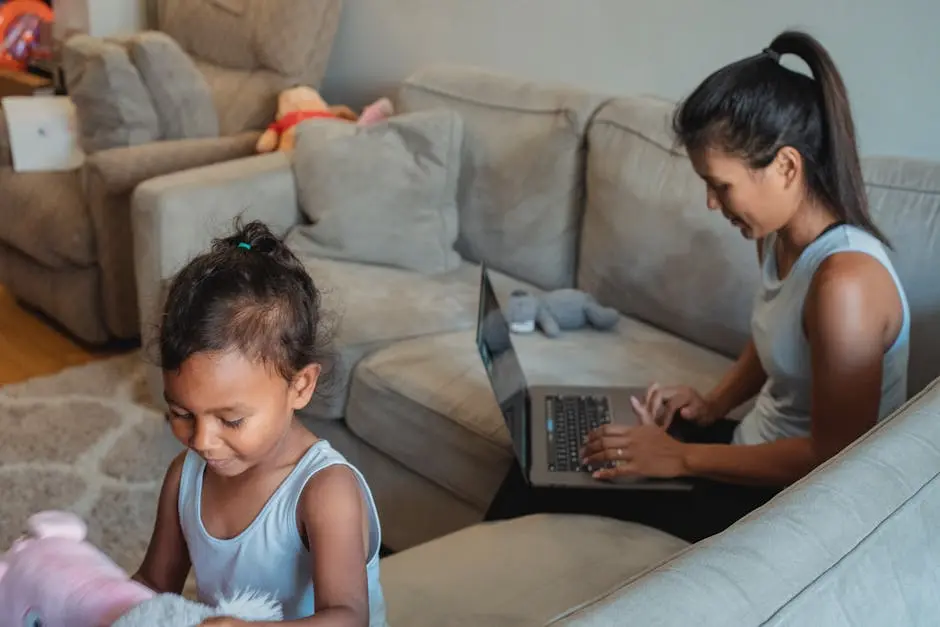 Adult mother using netbook for remote work while sitting on couch with little daughter playing with toys in living room