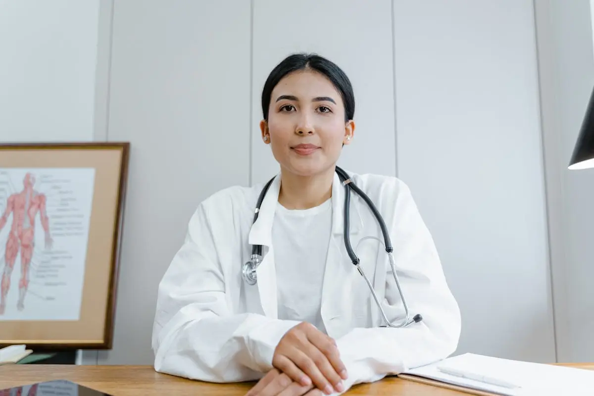 A female doctor confidently sits at her desk, ready for consultation in a medical office.