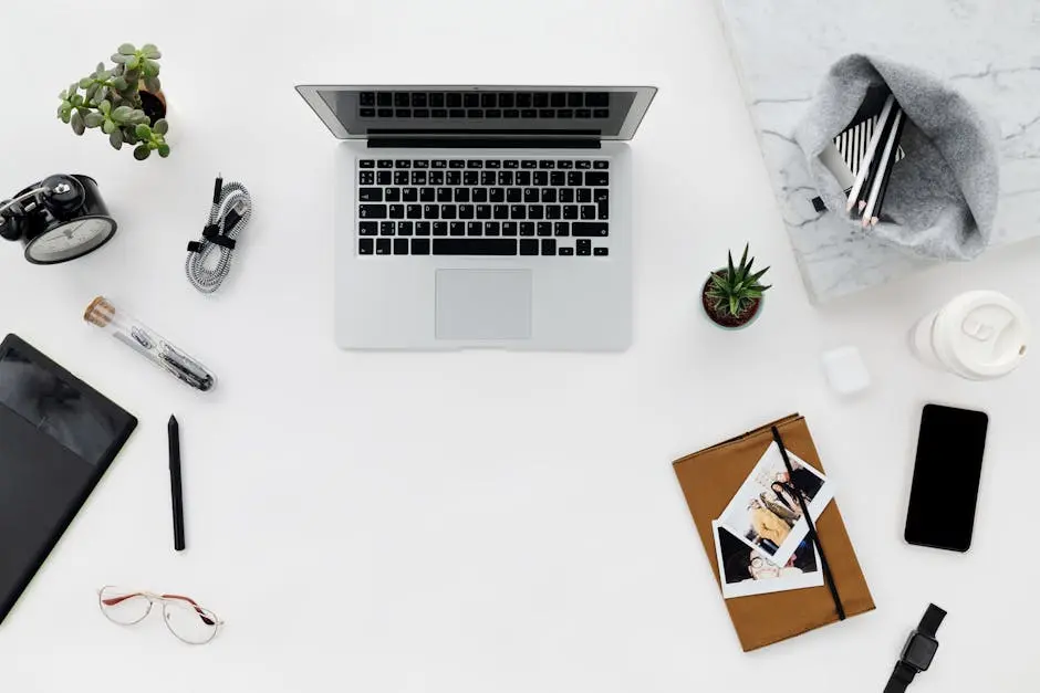 Top view of a minimalist workspace featuring a laptop, gadgets, and stationery on a clean desk.