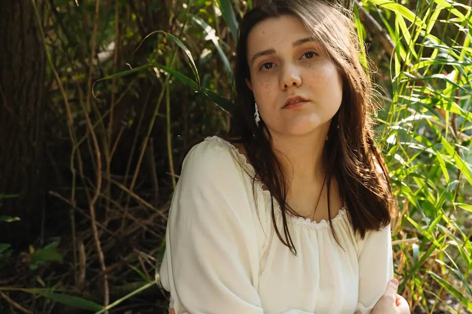 A contemplative young woman with freckles in a natural outdoor setting.