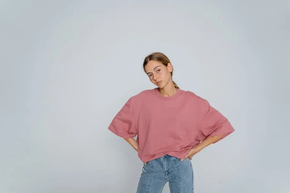 Portrait of a woman in a pink top and denim jeans posing with hands on waist.