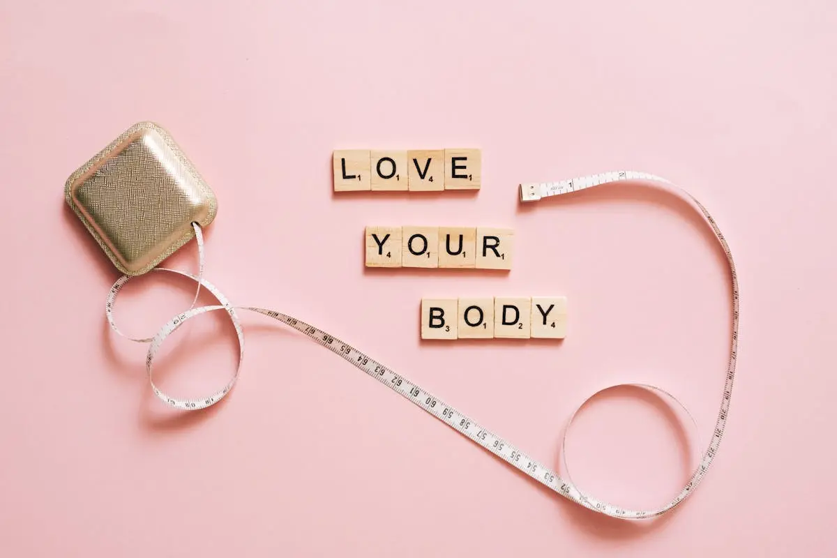 Scrabble letters spelling ‘Love Your Body’ with a tape measure on a pink backdrop.