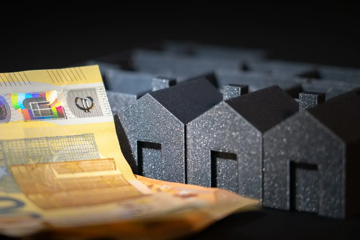 Close-up of black miniature houses with Euro notes, representing real estate investment and savings.