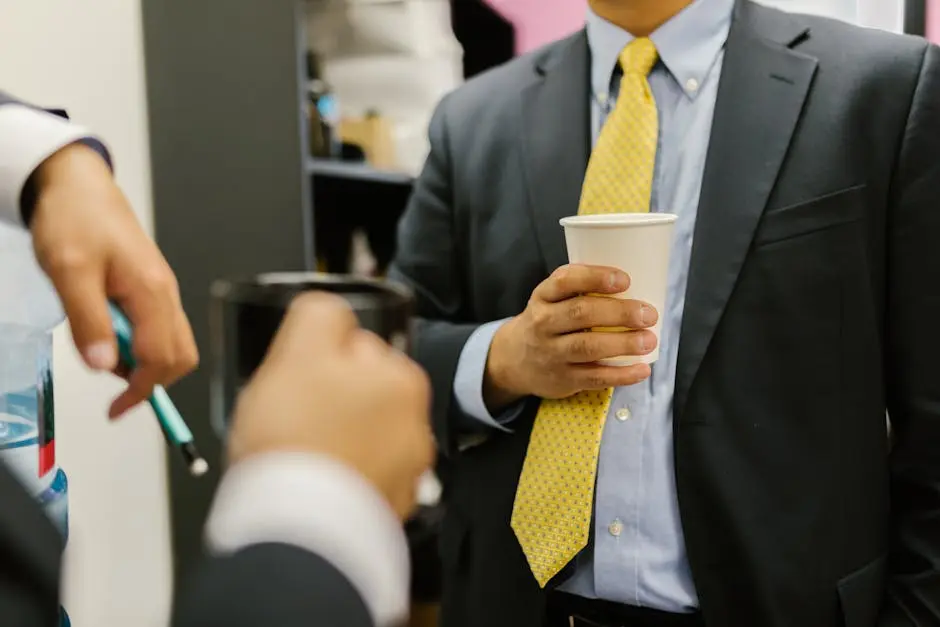 Close-up of business professionals networking, holding paper cups in office attire.