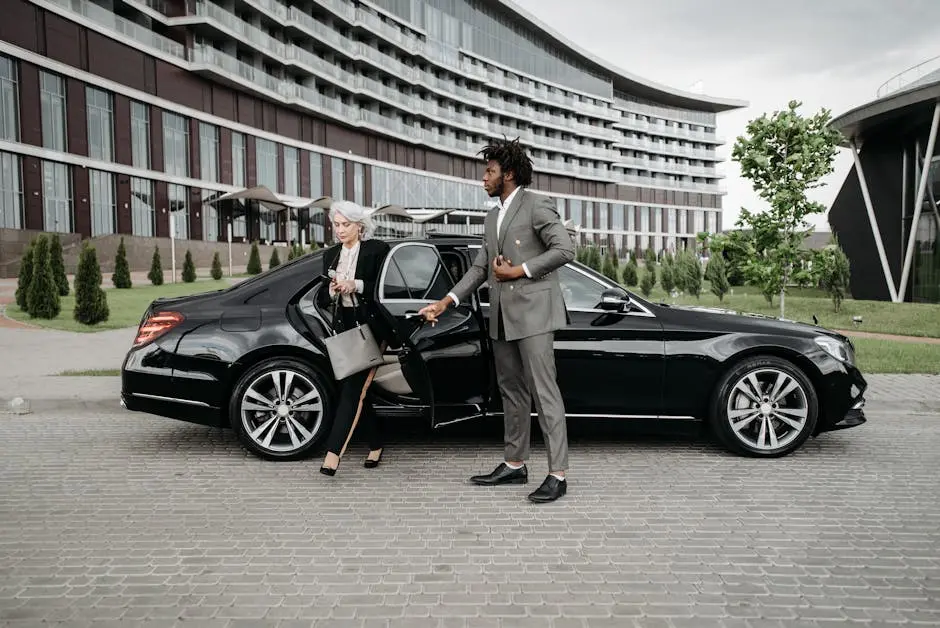 A professional chauffeur assists a businesswoman exiting a luxury car in front of a modern building.