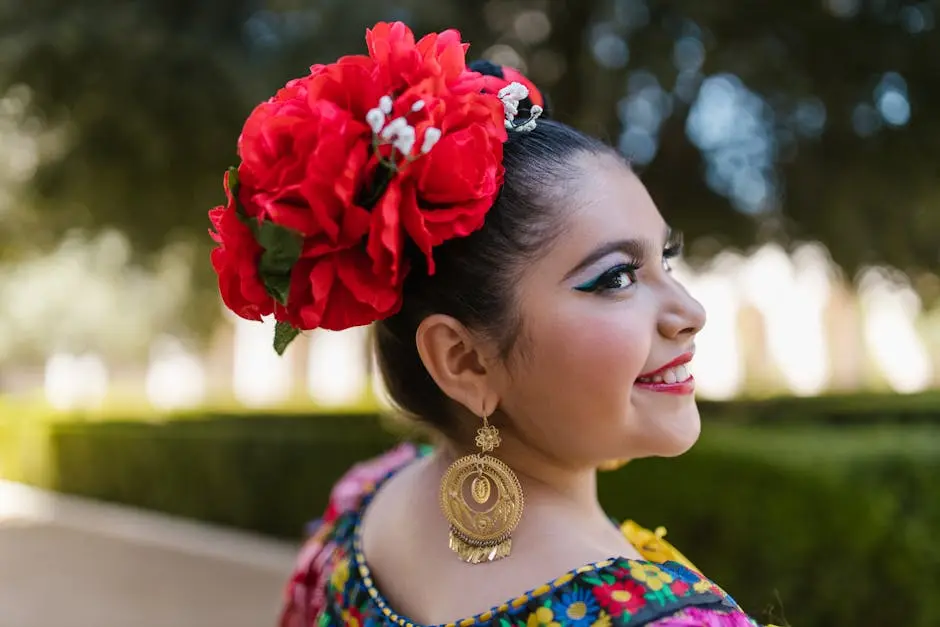 Smiling woman in traditional Mexican attire with red flowers, celebrating cultural heritage outdoors.