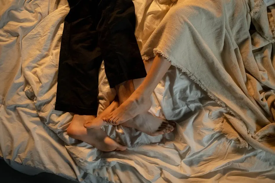 Close-up of a couple’s feet intertwined on a cozy bed, expressing intimacy and warmth.