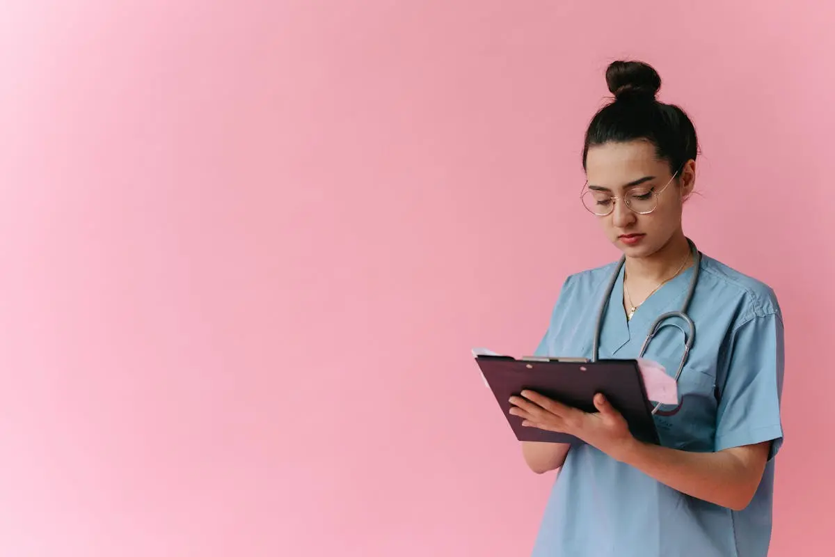 Professional nurse reviewing patient notes on clipboard with pink background, in studio setup.