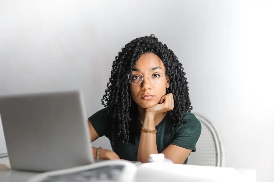 Young woman with glasses working attentively on a laptop at a bright desk.