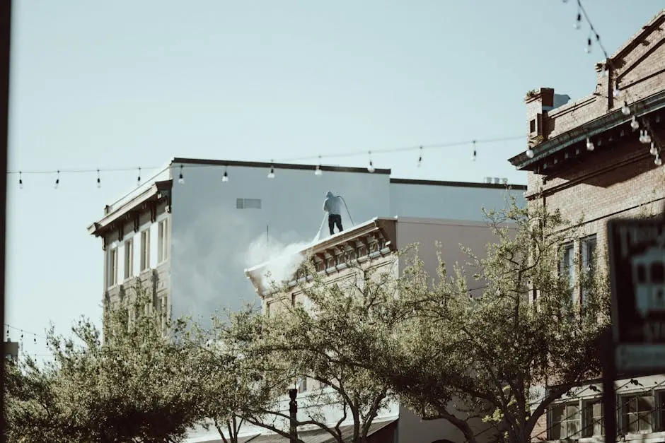 Rooftop worker using pressure washer in a cityscape with urban street below.