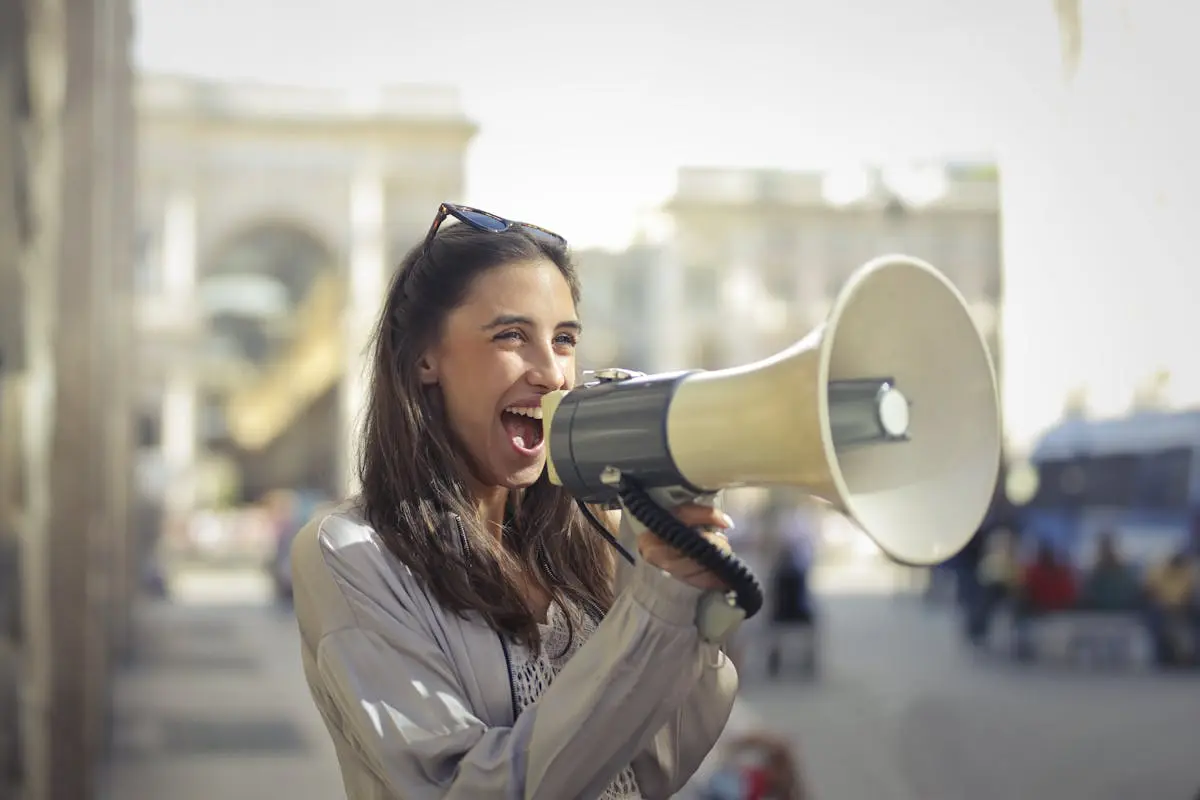 Cheerful young CMO in a casual outfit shouting into a megaphone on a sunny day.