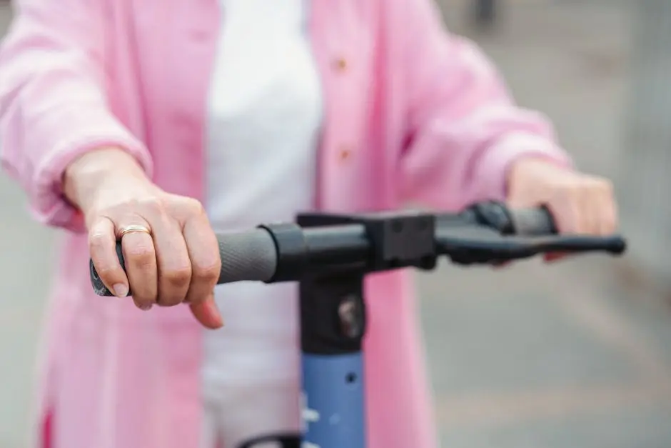 Hands gripping the handlebars of an electric scooter, wearing a pink jacket outdoors.