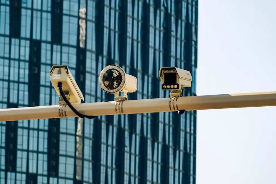 Surveillance cameras mounted on a pole in front of a modern glass building.