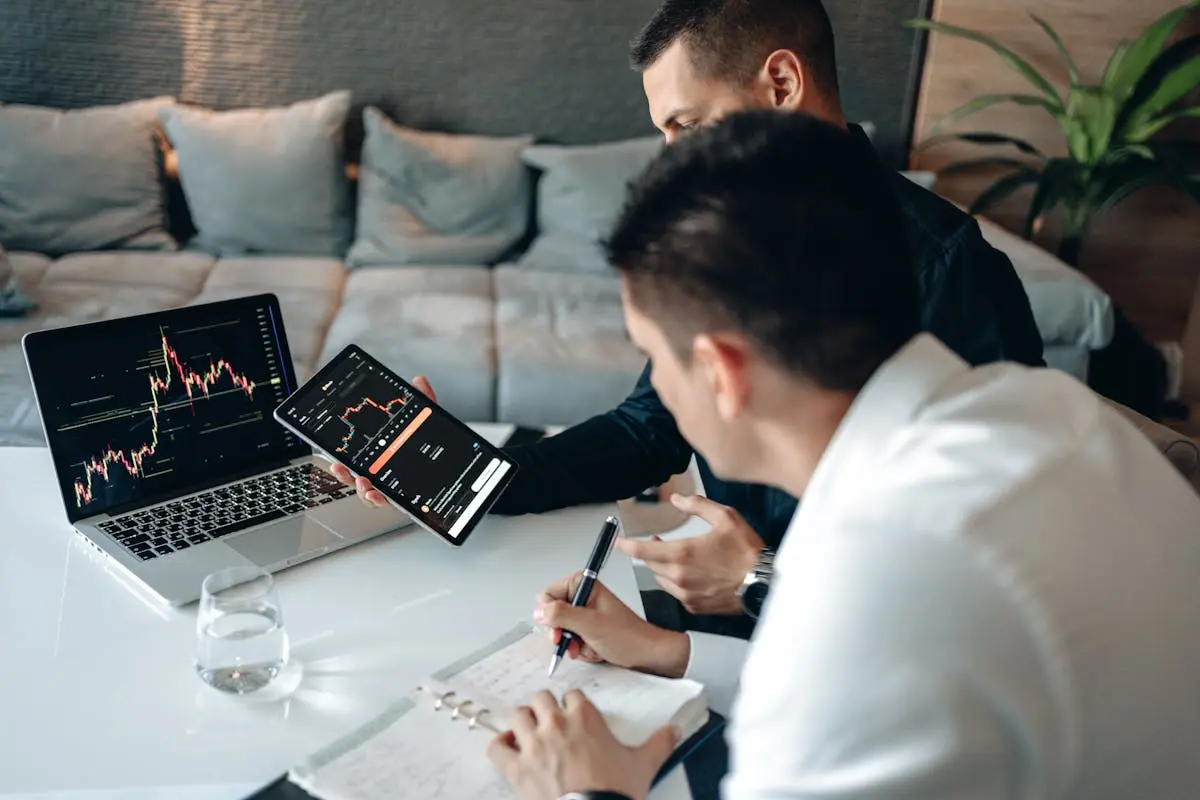 Two men business coach discussing market trends using a tablet and laptop in a modern office.