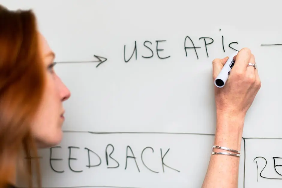 A woman writes &lsquo;Use APIs&rsquo; on a whiteboard, focusing on software planning and strategy.