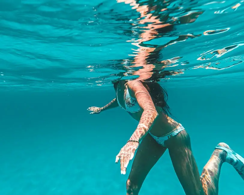 A woman swimming underwater in clear blue sea, sunlight reflecting on water.