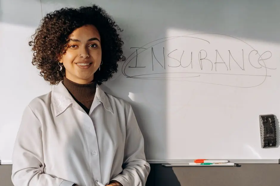 African American woman smiling in office setting with a whiteboard displaying ‘Insurance’.
