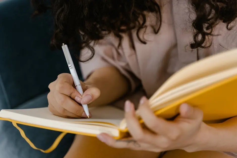 Person writing in a yellow notebook indoors, focusing on ideas.