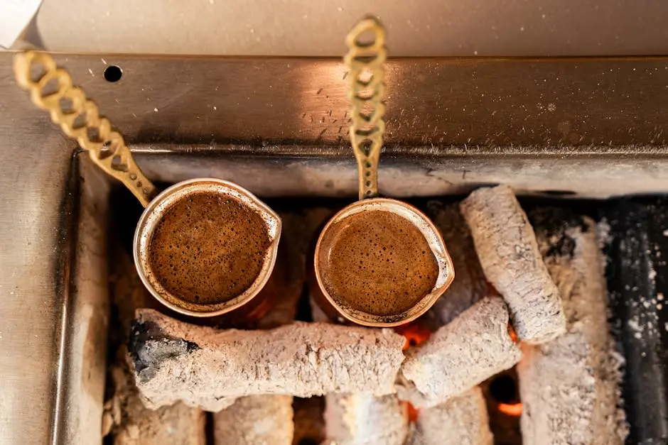 Two copper pots brewing Turkish coffee over hot coals, showcasing authentic preparation.