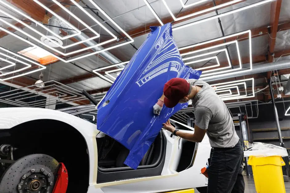Auto mechanic applying blue vinyl wrap to a car door in a modern garage.