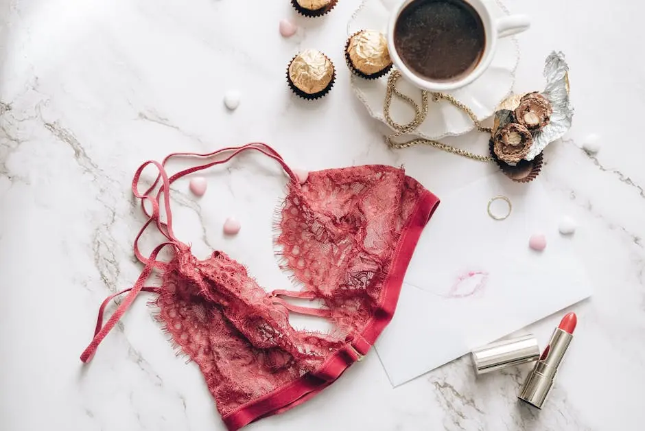 Stylish flat lay featuring red lace lingerie, coffee, chocolates, and lipstick on a marble surface.