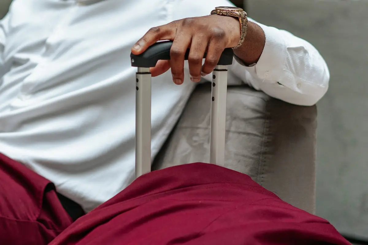 Close-up of a business traveler’s hand resting on a suitcase handle, dressed in casual attire.
