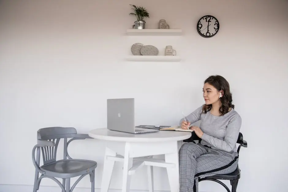 A young woman sitting at a desk with a laptop and notebook, studying at home.