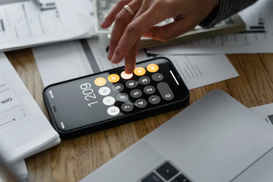 Close-up of a person using a smartphone calculator on a table with documents for financial calculations.