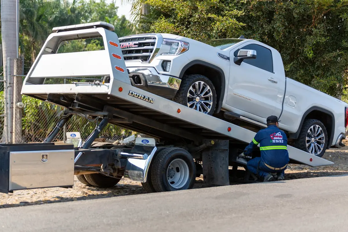 Tow truck operator loading white GMC pickup truck on street in daytime. liberty capitals